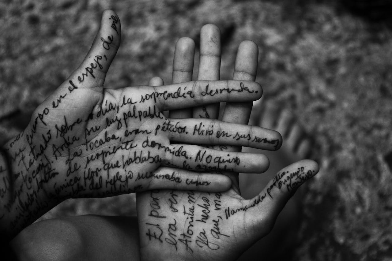 Artistic black and white photo of hands with handwritten text on skin.