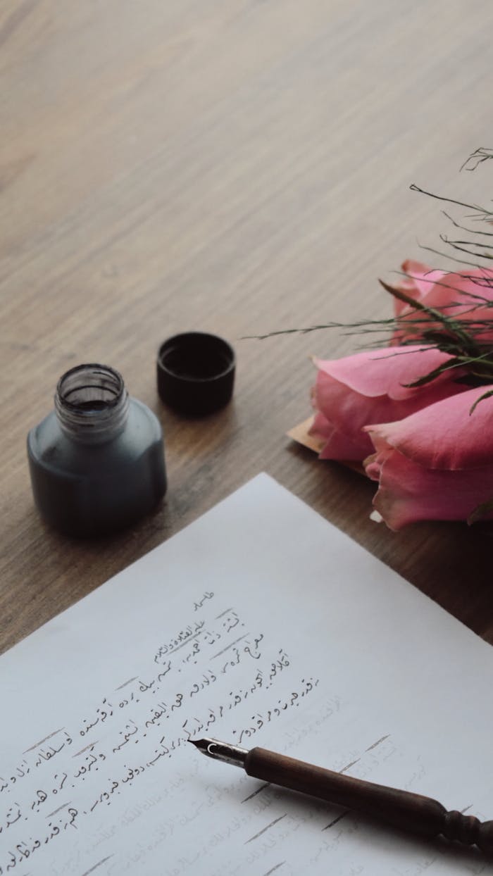 A beautiful display of calligraphy with ink and roses on a wooden desk, evoking elegance.
