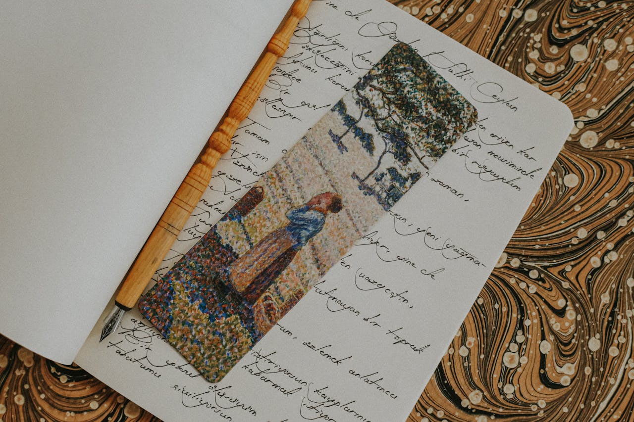 Open notebook with artistic bookmark, calligraphy, and wooden pen, evoking a vintage aesthetic.